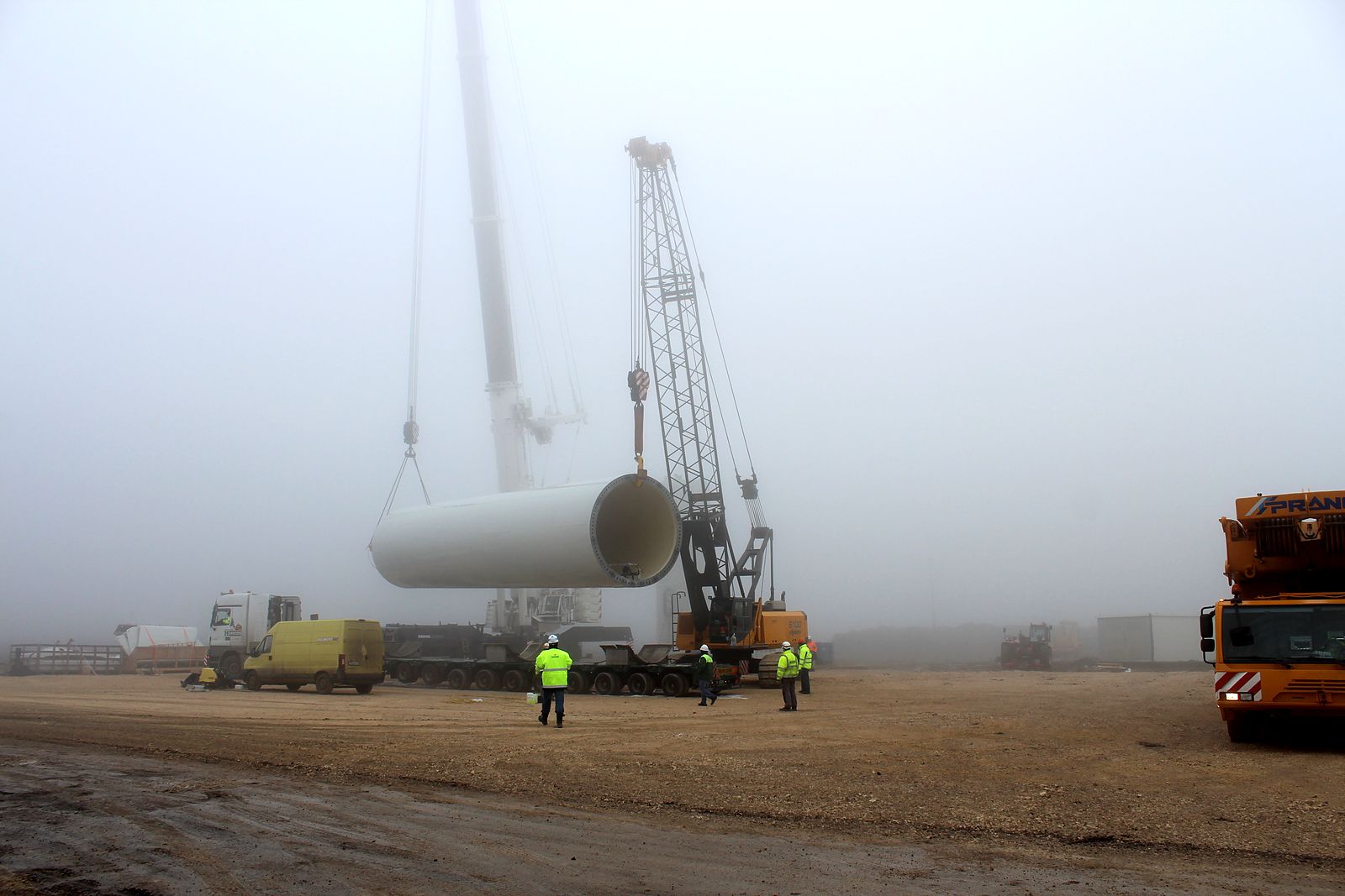 Tower section lifted through thick fog at Balchik Wind III, crew in hard hats and hi-vis