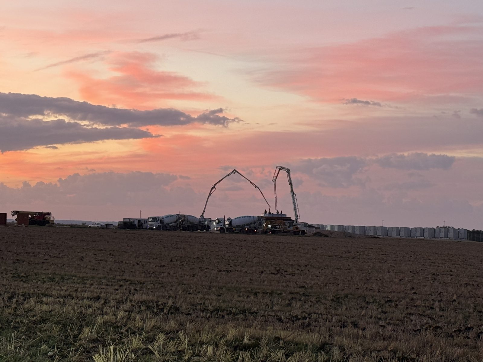 Concrete pumps at work on the Balchik Wind IV foundation, seen across the fields at dusk