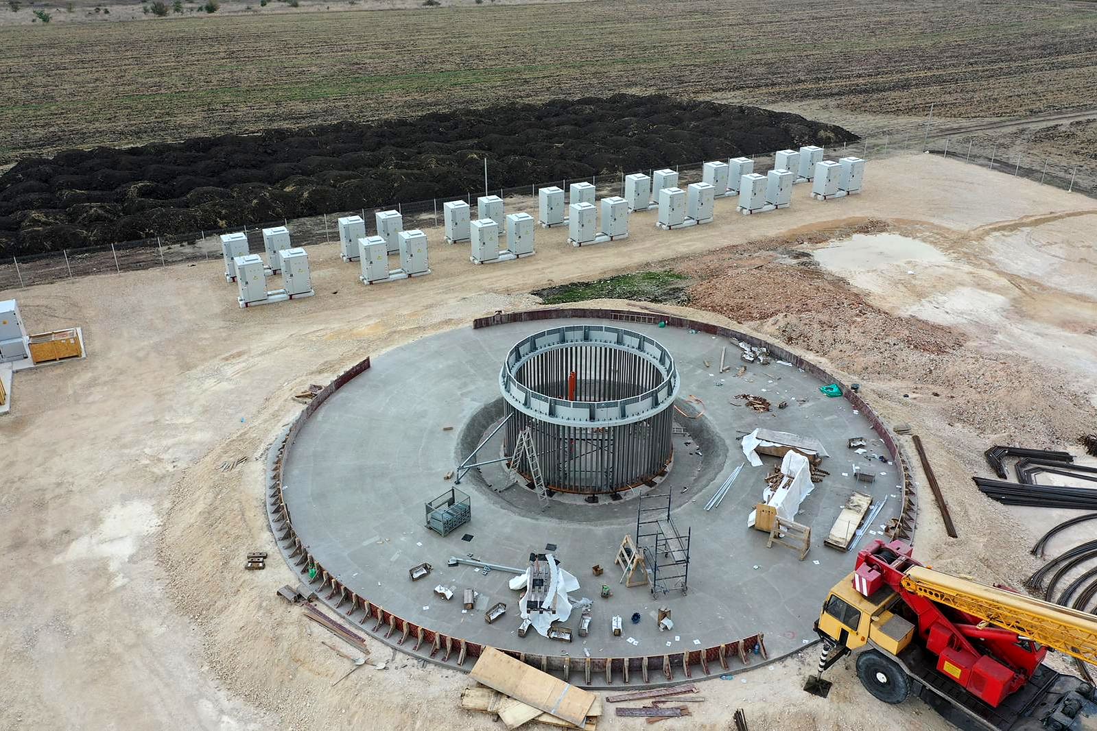 Drone view of the Balchik Wind IV foundation with its anchor cage, and battery cabinets lined up beside the pad