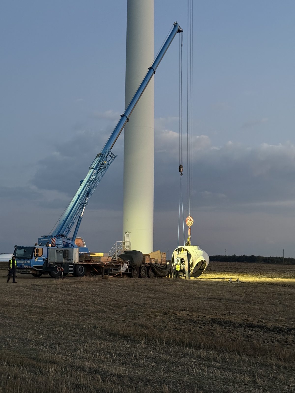 Mobile crane at the foot of a Balchik turbine tower in the evening light, with the rotor hub on the ground